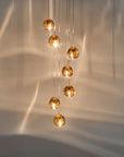 Terzani Mizu Pendant Light 7pcs cluster in champagne finish with water reflections on the wall. Available at Spacio retail stores in India.