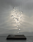 A cluster of Terzani Mizu Pendant Italian crystal light in clear finish above a floor coffee table with white pebbles showing water reflections on the wall. Available at Spacio retail stores in Mumbai & Kolkata.