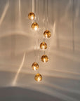 Terzani Mizu Pendant Light 7pcs cluster in champagne finish with water reflections on the wall. Available at Spacio retail stores in India.