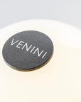 Round dark metal with 'VENINI' branding on a light gray background on the bottom of Fantasmino table lamp from Venini at Spacio store in Mumbai