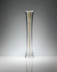 A tall, slender clear sculptural glass vase with a flared base, decorated with vertical gold leaf patterns, set against a gradient gray studio background.