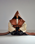 A handmade leather samurai sculptures, styled as a meditating or seated figure, featuring a brown textured leather hood and outer garments, cream-colored inner sleeves, and black leather lower body, set against a plain gray studio background.