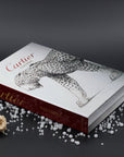 Assouline Cartier: Panthere coffee table book on a gray surface with pearls & roses decor at Spacio India for luxury home decor collection of Jewellery Coffee Table Books.