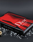Assouline Dior by Marc Bohan coffee table book on a grey back ground decorated with diamonds, pearls & white roses available at Spacio India for luxury home decor collection of Fashion Coffee Table Books.