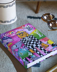 Assouline Louis Vuitton: Virgil Abloh Classic Cartoon Cover coffee table book on glass table with other home accessories available at Spacio India for luxury home decor accessories collection of Fashion Coffee Table Books.