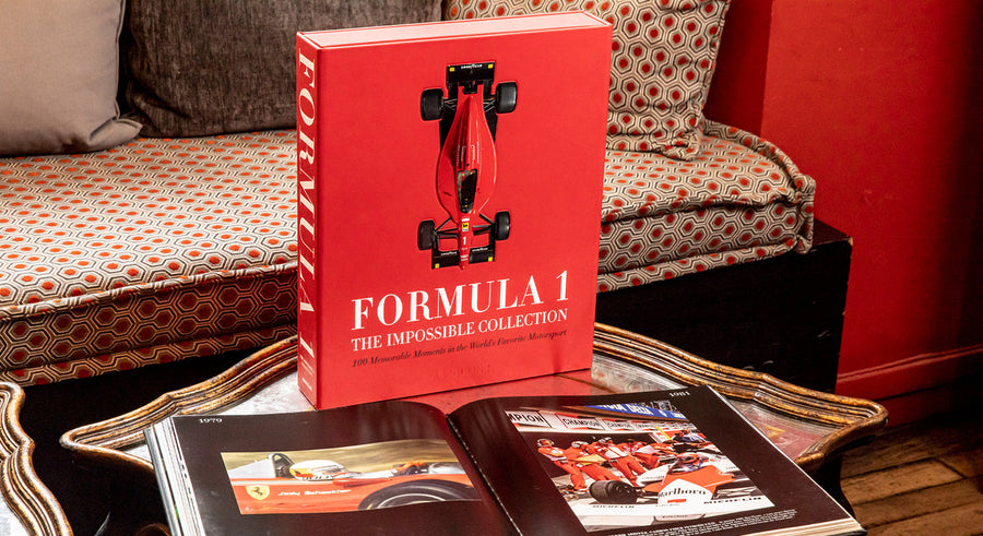 Assouline Formula 1: The Impossible Collection coffee table book on a coffee table with other opened book in a warm ambiance interior available at Spacio India for luxury home decor collection of Ultimate & Sports Coffee Table Books.