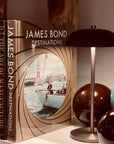 Assouline James Bond: Destinations coffee table book beside table lamp on console available at Spacio India for luxury home decor accessories collection of Travel Coffee Table Books.
