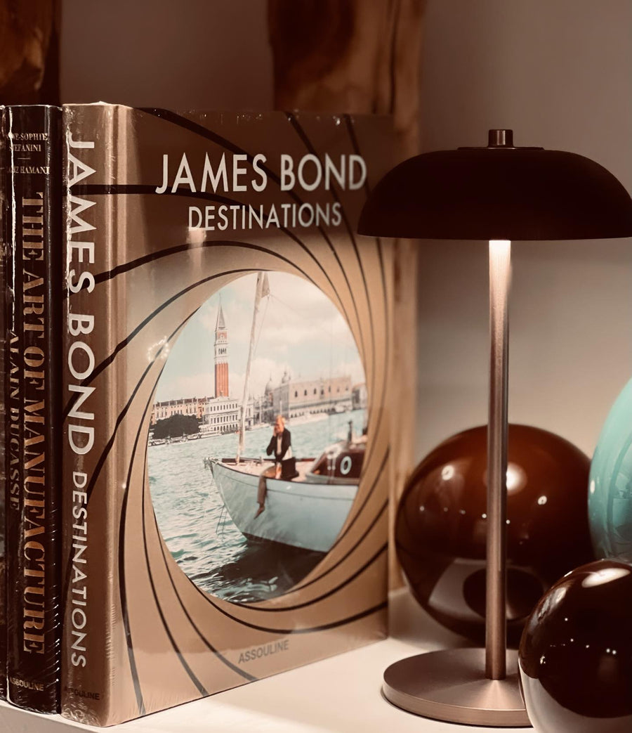Assouline James Bond: Destinations coffee table book beside table lamp on console available at Spacio India for luxury home decor accessories collection of Travel Coffee Table Books.