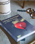 Assouline Louis Vuitton: Virgil Abloh Classic Balloon Cover coffee table book on glass table with other home accessories available at Spacio India for luxury home decor accessories collection of Fashion Coffee Table Books.