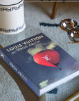 Assouline Louis Vuitton: Virgil Abloh Classic Balloon Cover coffee table book on glass table with other home accessories available at Spacio India for luxury home decor accessories collection of Fashion Coffee Table Books.