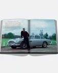 Open book showing a photo of a man standing next to a vintage car on a grassy field.