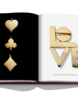 Assouline Cipullo: Making Jewelry Modern coffee table book displaying Cards symbols & Spelling L-O-V-E in 24 Gold caret on a coffe table available at Spacio India for luxury home decor collection of Jewellery Coffee Table Books.