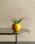 Yellow vase with pink flowers on a black table against a beige wall