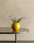 Yellow vase with pink flowers on a black table against a beige wall