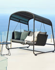 Cave Swing Sofa by Cane-line, designed by Jesper K. Thomsen, featuring a modern canopy design, soft cushions, and weather-resistant materials for indoor and outdoor use. Along with side table on a high rise building balcony in Mumbai