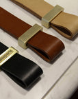 Three Esperia Eredania Horizontal leather belts with gold buckles on a marble counter.