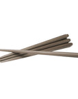Six long, slim taupe-brown sticks, likely wax taper candles, arranged in a crossed diagonal pattern on a solid white background by Ester & Erik, available at Spacio in India