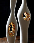 Two white and gold vases on a wooden table, including the Fos Ceramiche Falling in Love Gold Vase (Pair) by Enea Mazzotti.