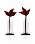 A pair of decorative glass floral sculpture with textured dark red flower heads and clear glass cylindrical stems on black square bases, photographed on a clean white background.
