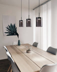 Modern dining room with a long wooden table and gray chairs, featuring pendant lights and a plant.