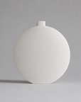 A minimalist matte white ceramic vase with a unique rounded, egg-shaped body and a short cylindrical neck, set against a solid neutral gray background.