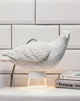 A peaceful white Lamp Haoshi Dove X Light 02 perched delicately on a table, bringing delight next to a book.