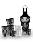 A set of sculptural drinking glasses and a decanter with a black and white mask face design, including two clear glasses, arranged on a white background.