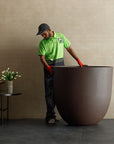 Person in a green shirt and cap moving a extra large planter in a room with a beige wall, available at Spacio retail stores in Mumbai & Kolkata.