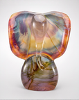 A sculptural glass Ganesh figurine with a calcedonio finish featuring swirls of orange, purple, blue, and gold, set against a clean light gray background.