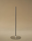 A minimalist, polished silver metal stand with a single vertical stem and a circular base, set against a solid warm beige background.