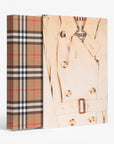 Slip case and hard cover in linen. Burberry coffee table book by Assouline, celebrating 165 years of British style, iconic trench coats, and timeless luxury through stunning illustrations and stories.