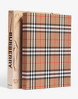 Hardcover and slip case in linen. Burberry coffee table book by Assouline, celebrating 165 years of British style, iconic trench coats, and timeless luxury through stunning illustrations and stories.