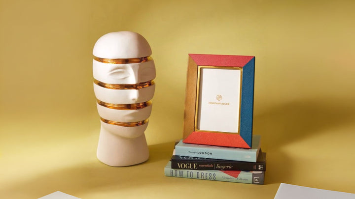 Jonathan Adler Atlas Sliced Bust Gilded styled with a photo frame on books on a mustard background, available at spacio india online and retail stores