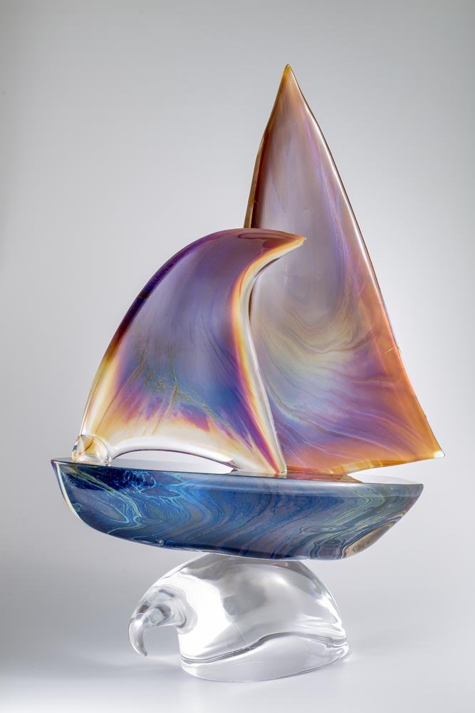 Full view of The Sail Murano glass sculpture, showing its sweeping coloured sails and crystal-clear wave-like base, available at Spacio India.