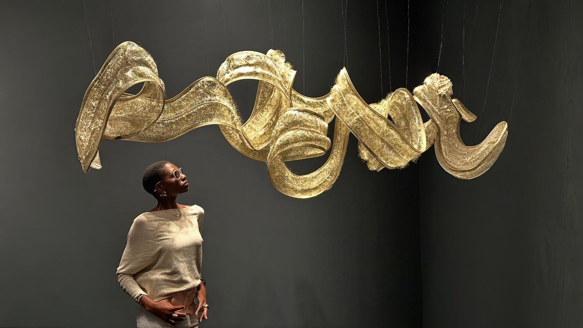Terzani Metal fabric light sculpture in gold finish installed from the ceiling and a lady admiring the light. 