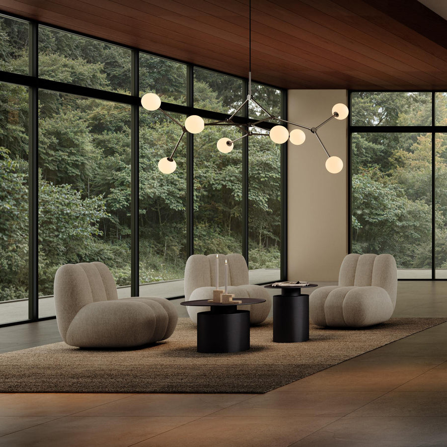 Modern living room with large windows, beige chairs, and a chandelier.
