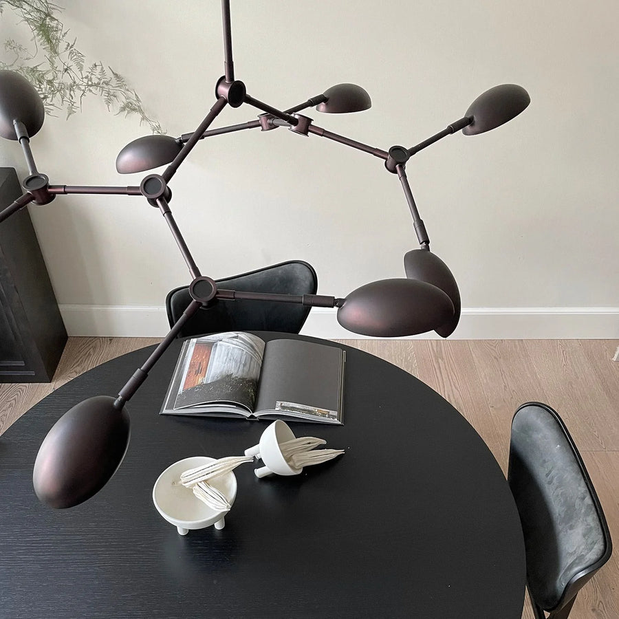 A modern chandelier hanging from the ceiling on a dining table styled with coffee table books and bowls. 