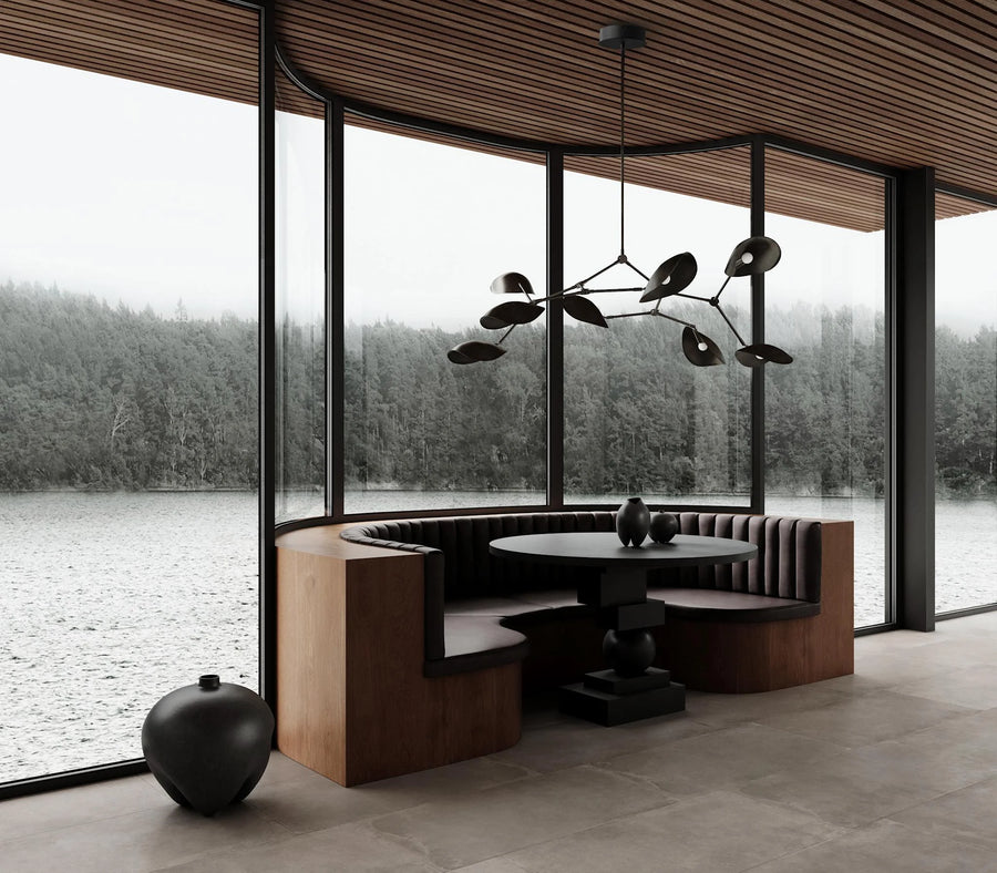 Modern interior with a round table and bench seating by large windows with a view of water and trees.