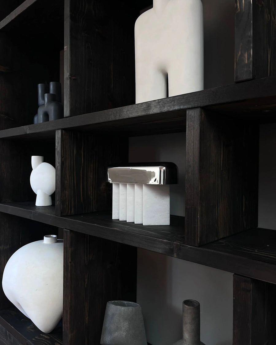 Dark wooden shelves with various white ceramic vases and objects against a black background