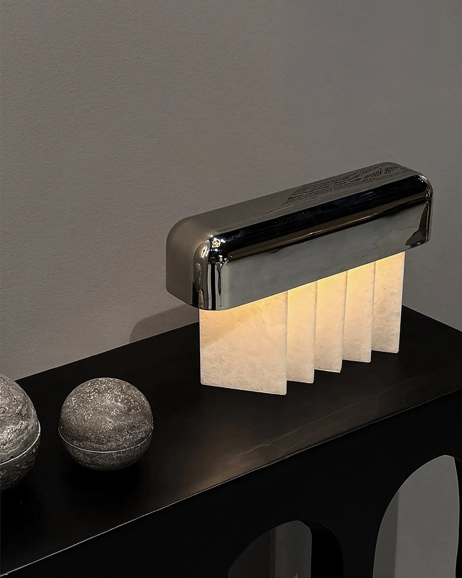 Modern table lamp with a metallic base and crystalized marble panels on a dark surface.