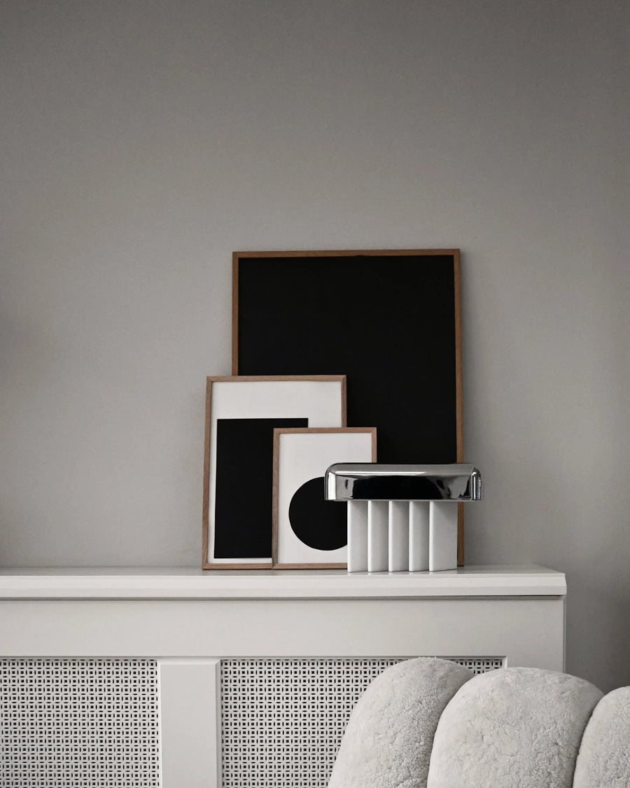 Framed artworks on a shelf against a gray wall with a textured surface.