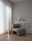 Modern gray armchair in a minimalistic room with light-colored curtains and wooden floor.