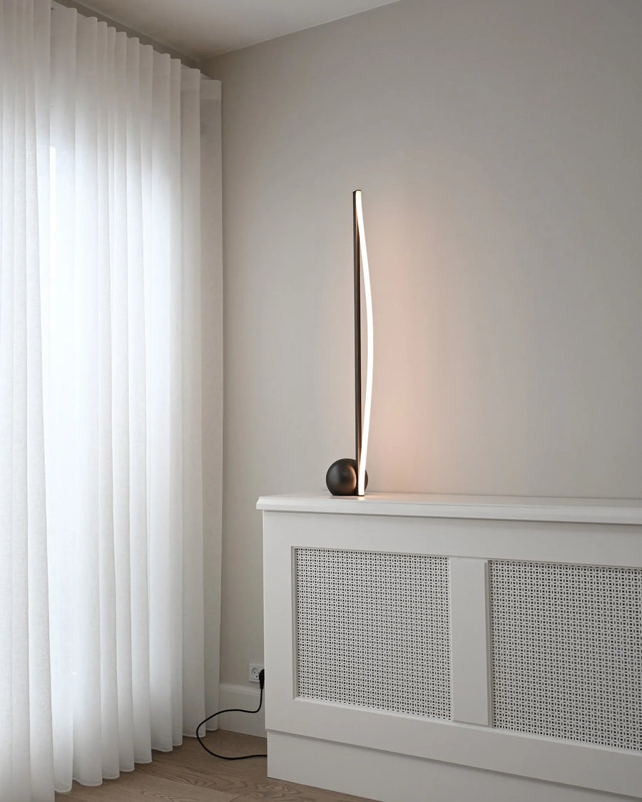 Modern floor lamp on a white radiator with white curtains in the background