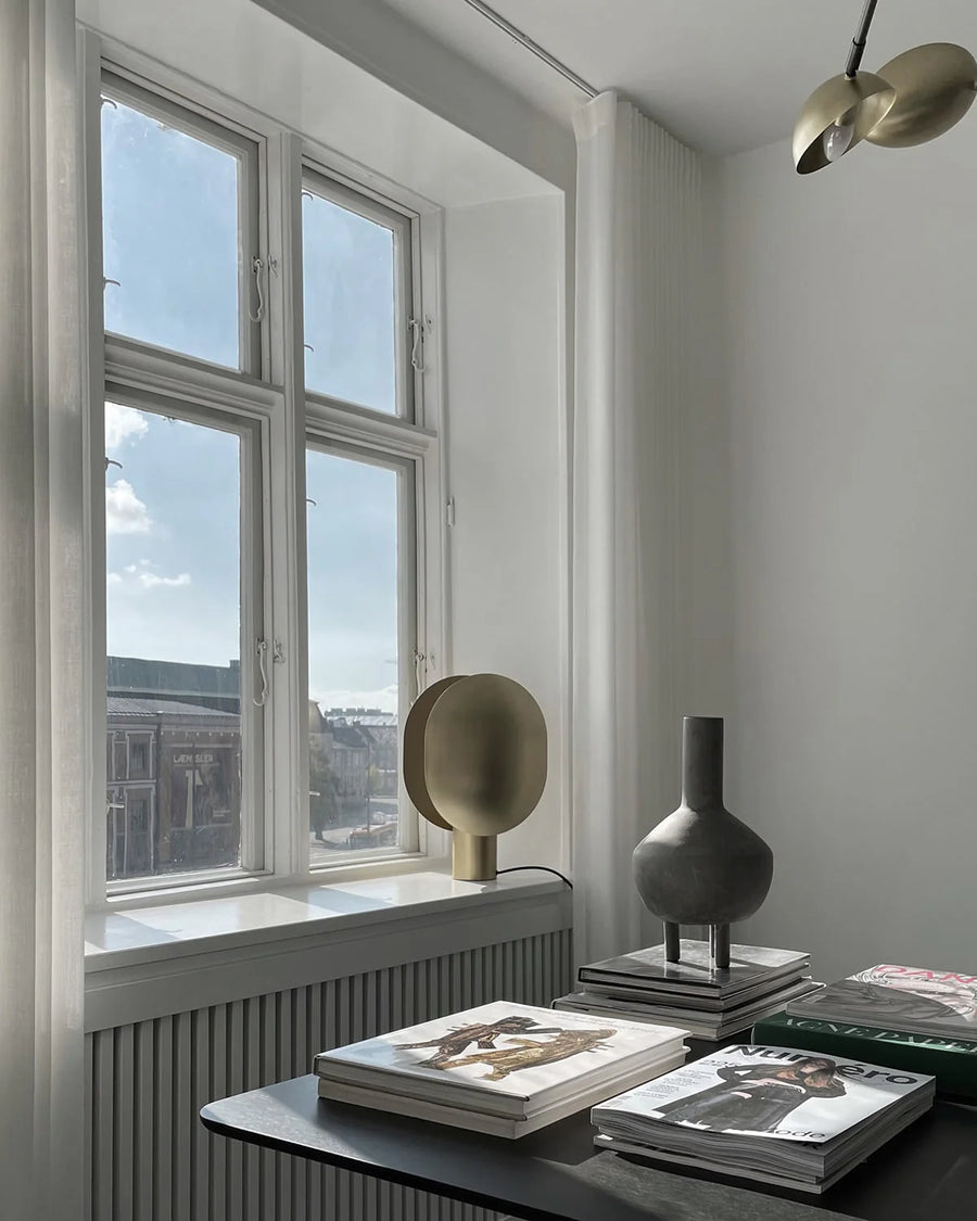 Modern interior with a window, books, and a minimal sculptural vase on a table.