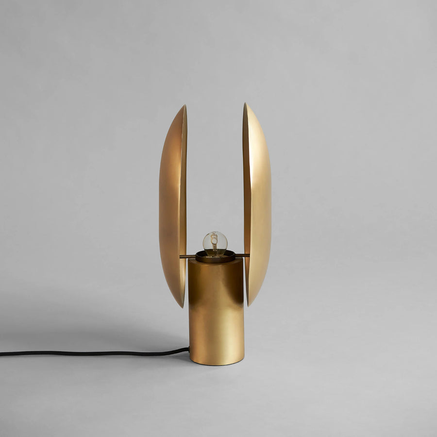 Side view of a brass table lamp with unique design on a gray background, from 101 Copenhagen available at Spacio retail stores in Mumbai & Kolkata. 
