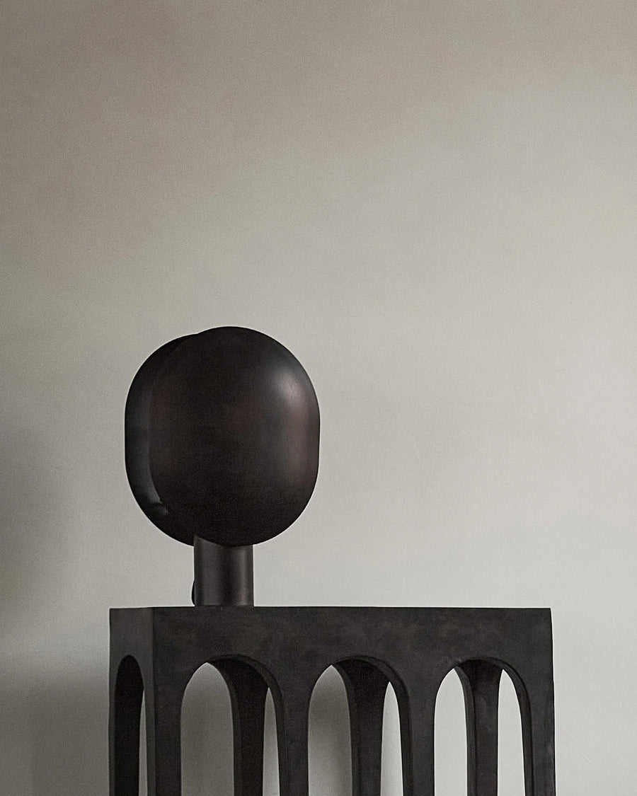 Dark metal sculptural table lamp with spherical top on a plain background