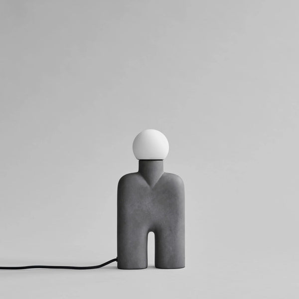 Modern & minimal table lamp with a gray base and white bulb on a light gray background from 101 Copenhagen available at Spacio retail stores in Mumbai & Kolkata. 