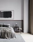 Modern bedroom with gray bedding, abstract art on the wall, and a side table.