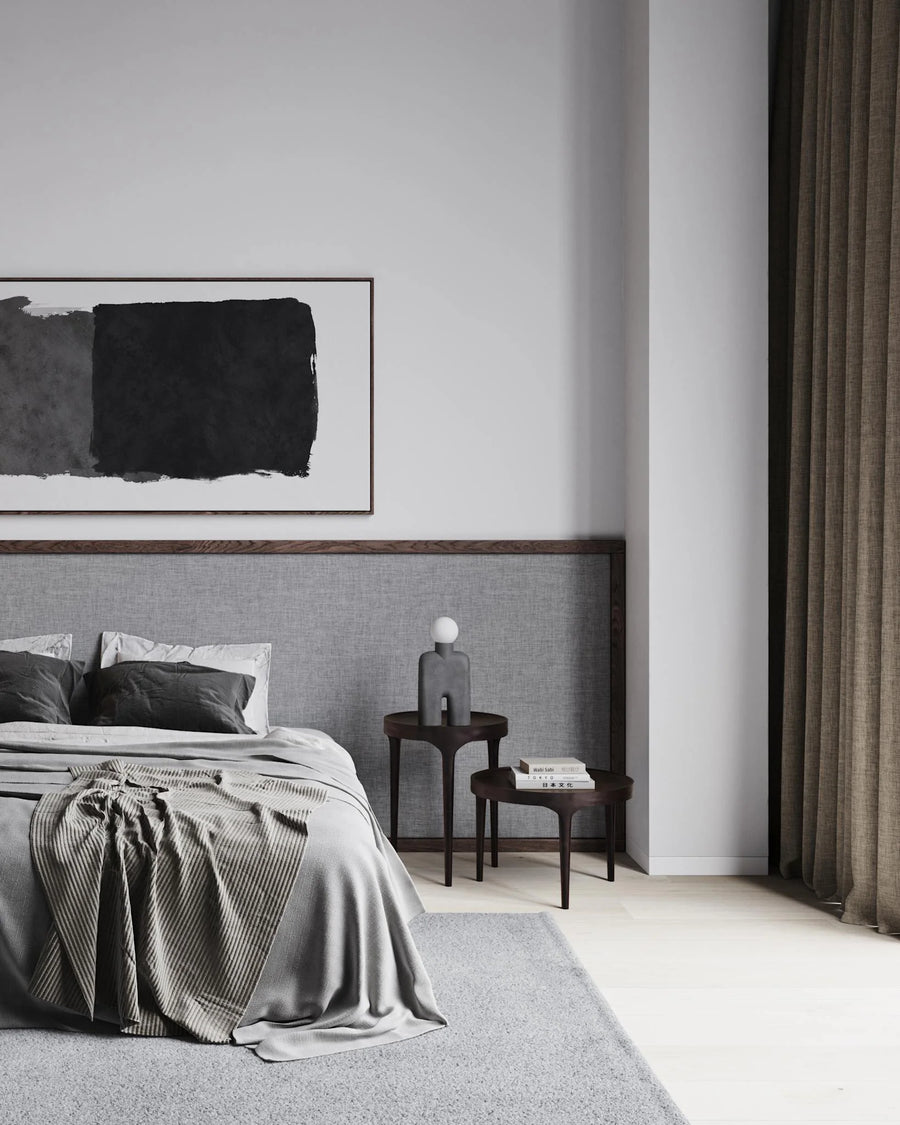 Modern bedroom with gray bedding, abstract art on the wall, and a side table.
