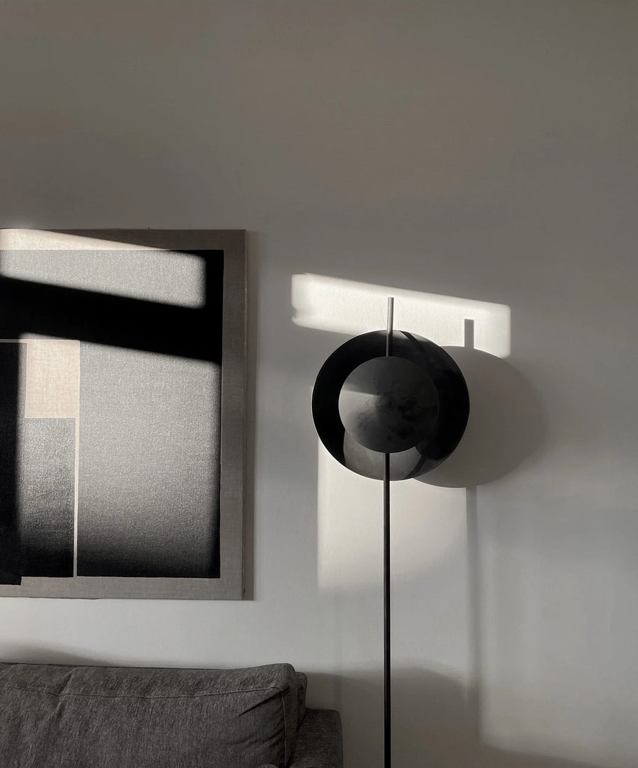 Modern black floor lamp in a minimalistic room with abstract art on the wall.